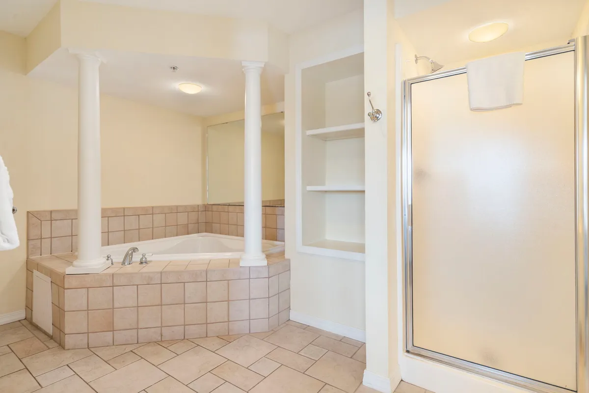 A serene bathroom retreat with a luxurious jacuzzi-style soaker tub, a spacious enclosed shower, elegant pillars, and neatly arranged shelves for towels and amenities. The space exudes a spa-like tranquility, perfect for unwinding after a long day.