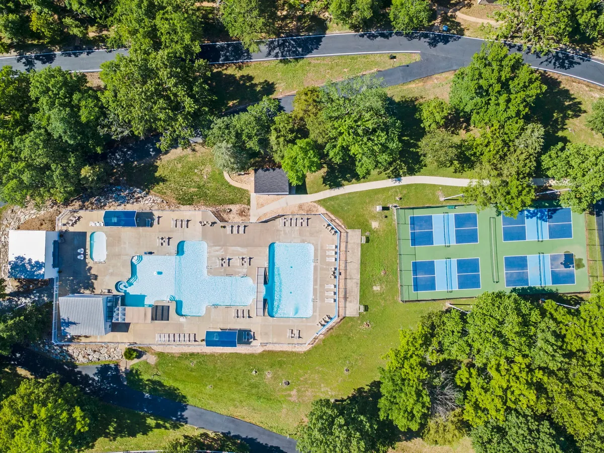 This exterior shot showcases a swimming pool and tennis courts nestled amid vibrant greenery. The pool area is set up for both sunbathing and swimming, while the courts offer additional recreation options. The overall mood is relaxed and recreational, highlighting the resort-style amenities available to guests.