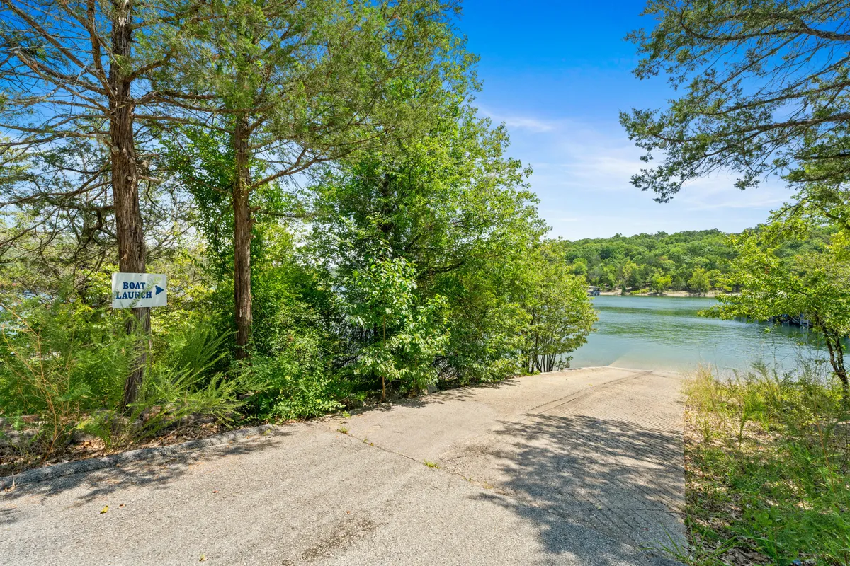 A tranquil lakeside scene with a boat launch sign overlooking a calm river, surrounded by verdant greenery. The area invites guests to embark on boating or fishing adventures and provides easy access to the water.