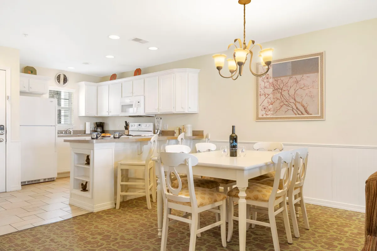 The image showcases a beautifully appointed open-concept dining area with a stylish dining table, modern kitchen island, statement chandelier, and elegant wall art. The setting exudes warmth and comfort, inviting guests to gather for shared meals or celebrations.