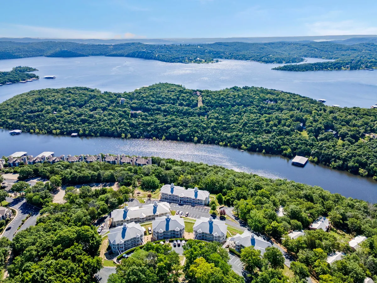 A tranquil view of Table Rock Lake framed by rolling hills and residential buildings, with a spacious dock extending into the water. The scene suggests opportunities for boating, fishing, and lakeside picnics, while the calm water reflects the sky and surrounding nature.