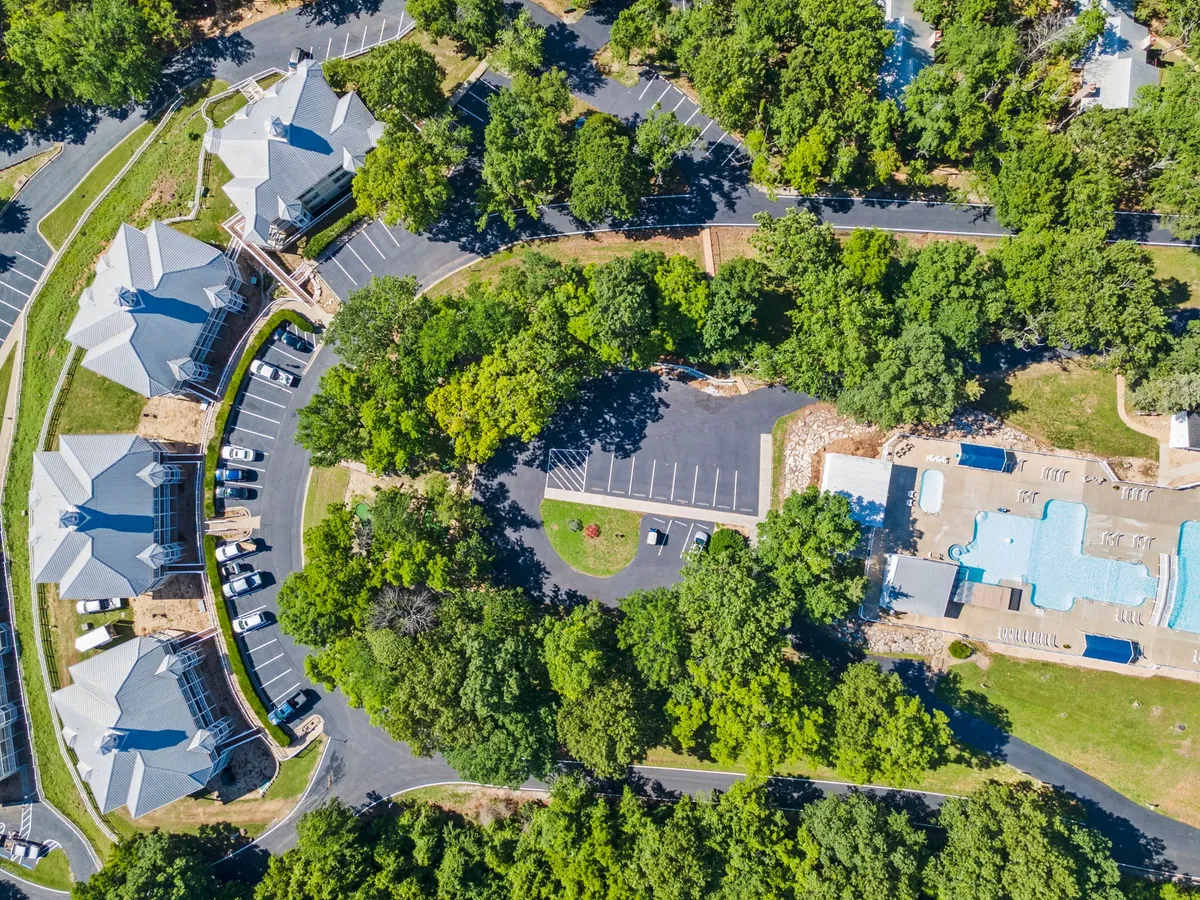 A vibrant scene featuring a large, inviting outdoor pool surrounded by lounge chairs, landscaped greenery, and a cluster of resort buildings. Families and friends can be seen enjoying the poolside, while the surrounding area hints at additional recreational amenities and social spaces.