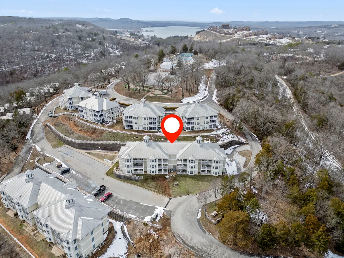 This image features a cluster of condo buildings nestled in lush greenery, with the lake visible in the background. Grassy areas and walking paths are apparent, offering a peaceful, open environment ideal for outdoor activities. The natural setting is inviting and highlights the proximity to the lake.