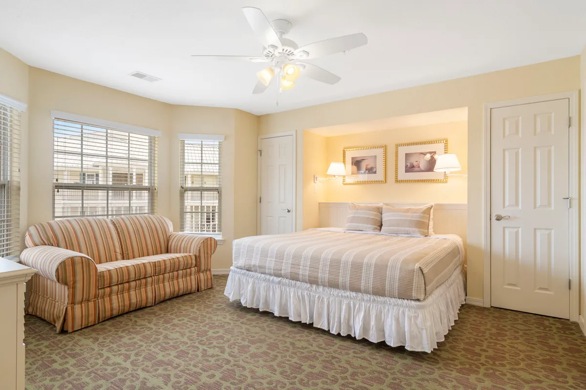 A bright, comfortable bedroom with a neatly made bed with striped bedding, a cozy sofa, wall art, and soft lighting. The room is spotless, radiating a sense of calm and relaxation, perfect for a restful stay.