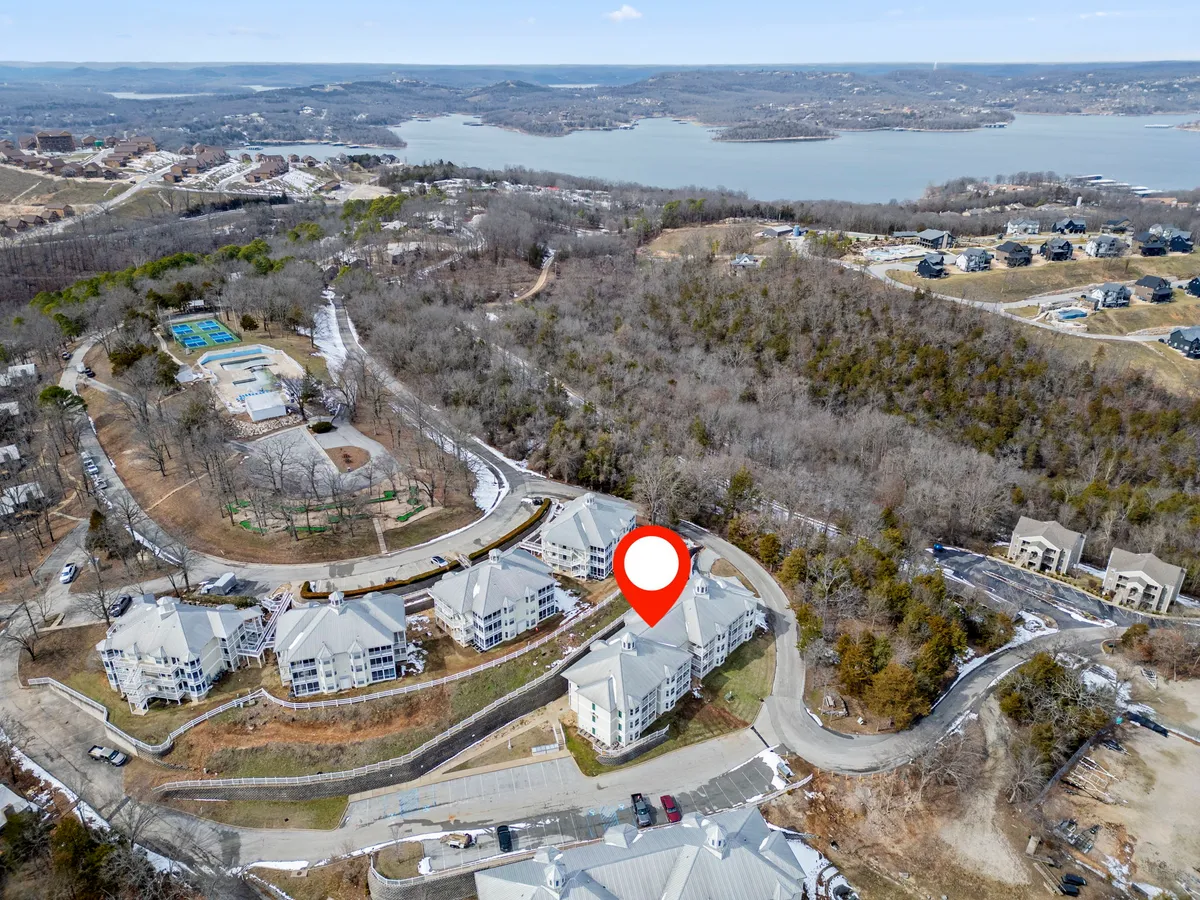 This image features a scenic exterior view showcasing residential buildings nestled beside a sparkling swimming pool, with Table Rock Lake visible in the background. The setting evokes a sense of community, relaxation, and outdoor adventure. People are seen swimming, relaxing by the lake, and engaging in community activities, all under a warm sunset glow.